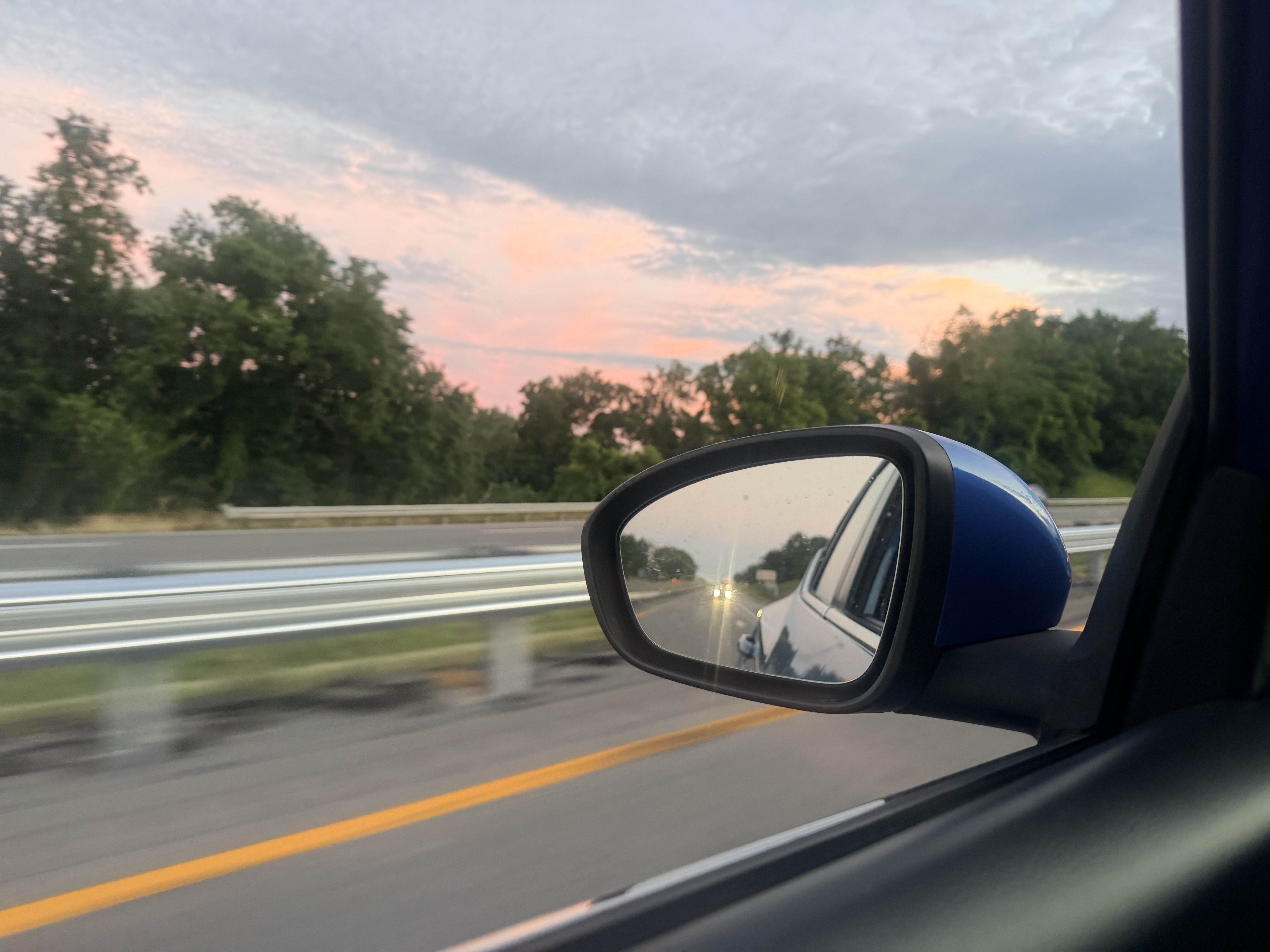 A view of the road ahead reflected in the car's side mirror during the drive.