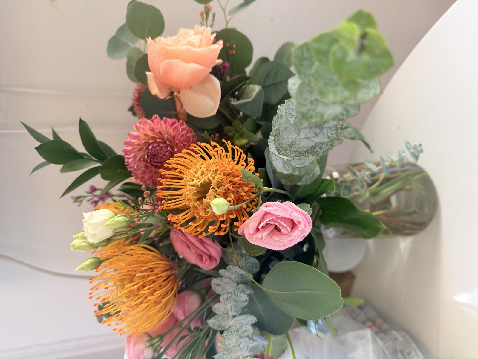 A bouquet of pink roses, orange pincushion protea, magenta dahlias, a cream rose, and eucalyptus in a glass vase, sent by the author's mom during her stimulation cycle.